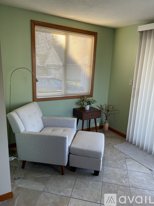 A living room with a chair, ottoman, and a small table with a plant on it.