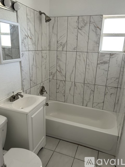 A bathroom with a marble tile wall and a white bathtub.