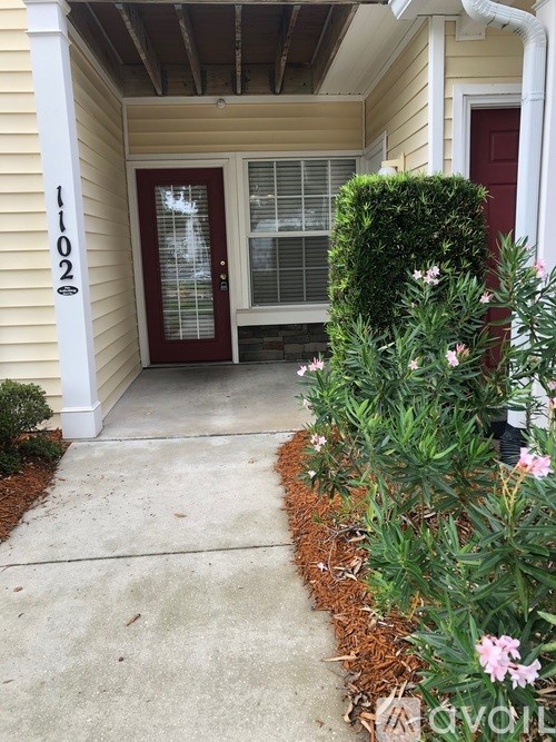A red door with a glass window is on the right side of a yellow house.