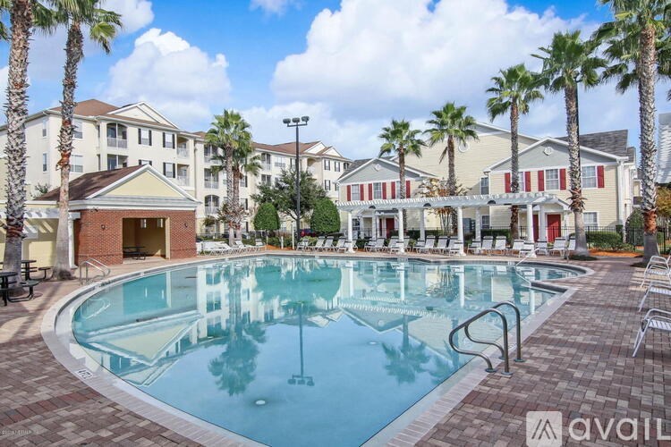A large swimming pool surrounded by palm trees and lounge chairs in front of apartment buildings.