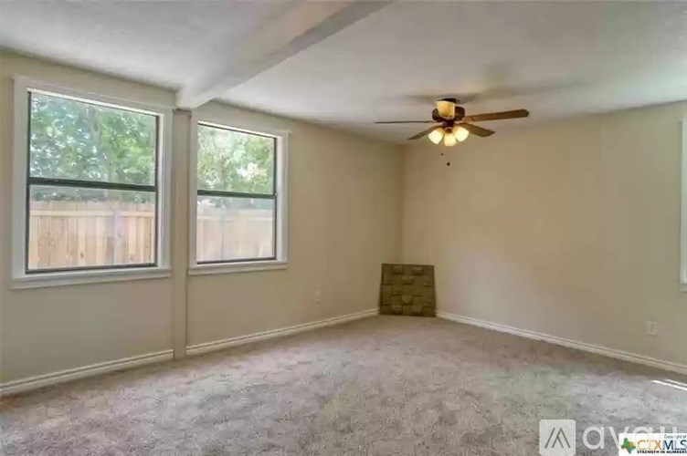A room with a ceiling fan and two windows.