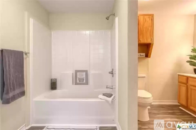 A white bathroom with a toilet, tub, and wooden cabinetry.