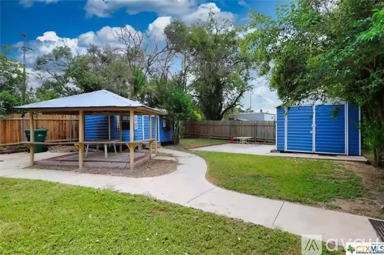 A gazebo is surrounded by a wooden fence and a blue storage unit.