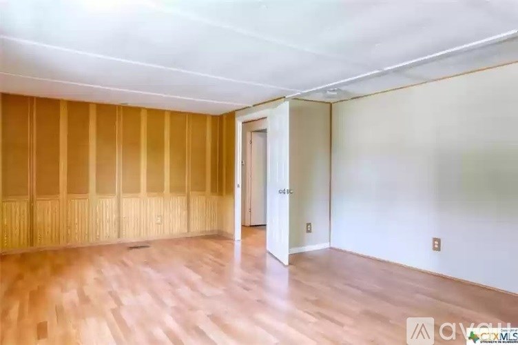 A room with wooden flooring and a door on the right side.