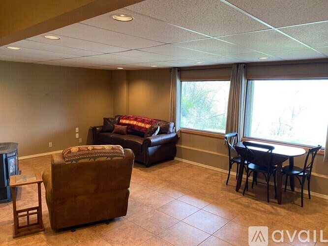 A living room with a brown sofa, a brown armchair, a small table, and a dining table with chairs.