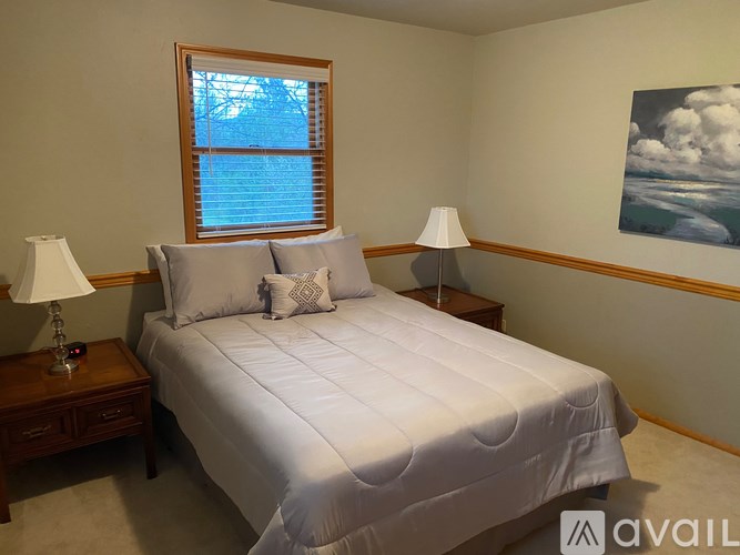 A bedroom with a large bed, two lamps, and a painting on the wall.