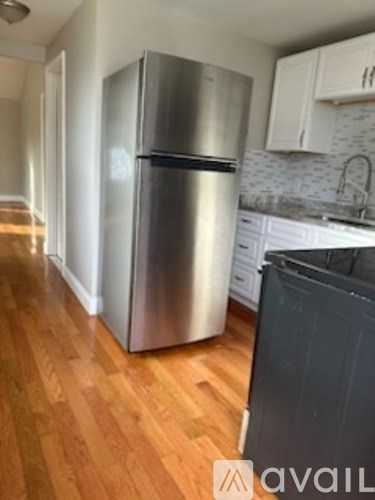 A stainless steel refrigerator in a kitchen with wooden floors.