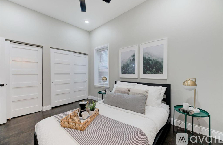 A bedroom with a bed, a basket on the bed, a side table with a lamp, and two framed pictures on the wall.