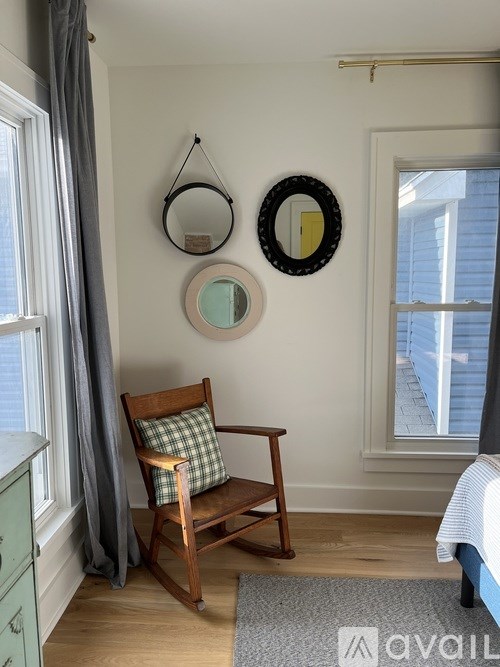 A wooden chair with a green pillow sits in a room with a mirror and a window.