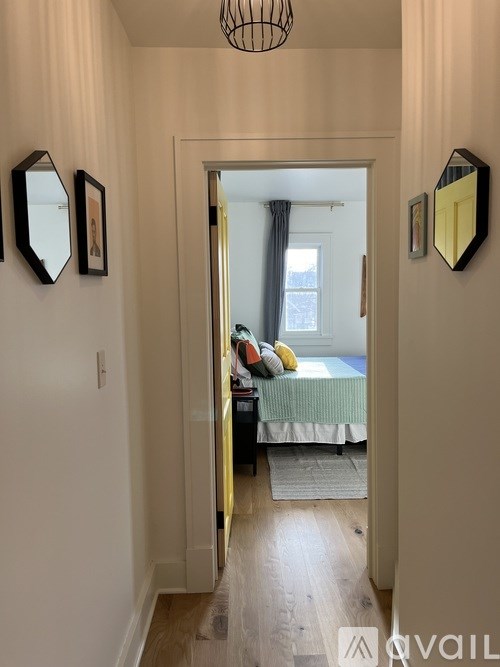 A hallway with a mirror on the wall and a bedroom at the end.