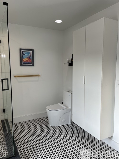 A white toilet sits in a bathroom with a black and white floor.