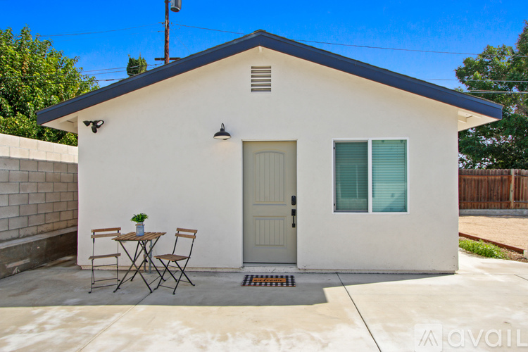 A small white house with a grey roof and a small patio with a table and two chairs.