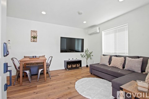 A living room with a grey couch, a wooden dining table with chairs, a flat-screen TV, and a rug.