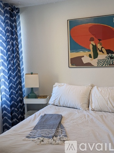 A bedroom with a bed, a nightstand with a lamp, and a framed picture on the wall.