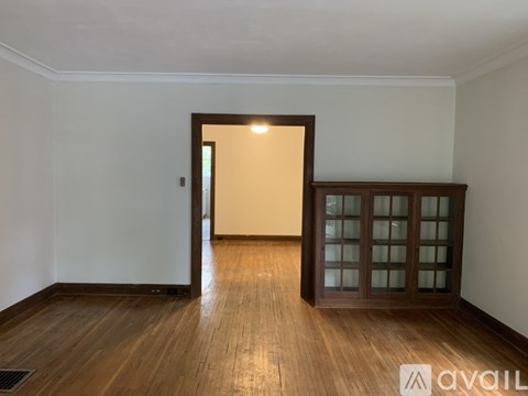 A room with wooden floors and a white wall with a doorway leading to another room.