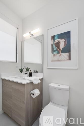 A bathroom with a toilet, sink, mirror, and a picture on the wall.