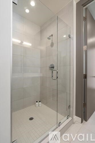 A glass shower stall with a glass door and a white tiled floor.