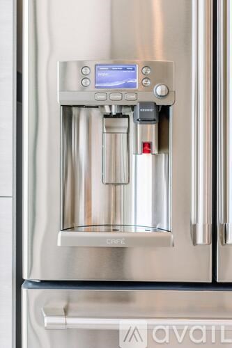 A stainless steel water dispenser with a digital display is mounted on a wall.