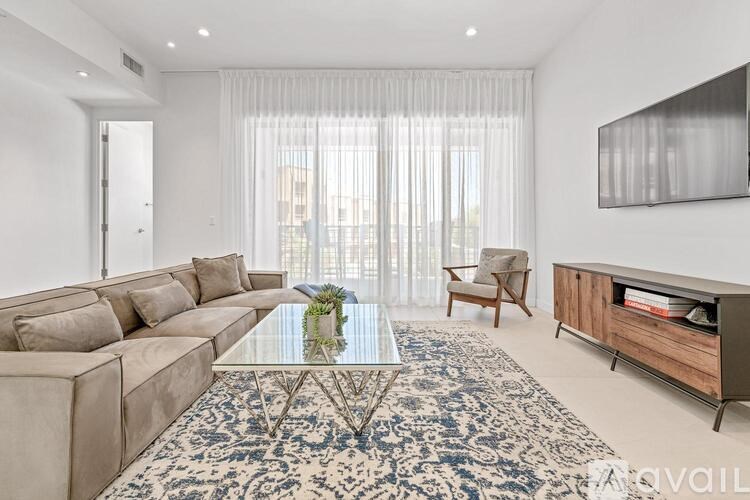 A living room with a beige sofa, a glass coffee table, and a large window with curtains.
