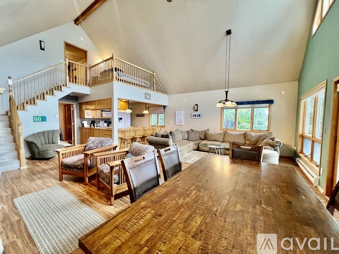 A large wooden table is in the middle of a spacious room with a staircase and a balcony.