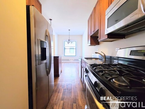 A white door opens to a small room with a wood floor and a white refrigerator.