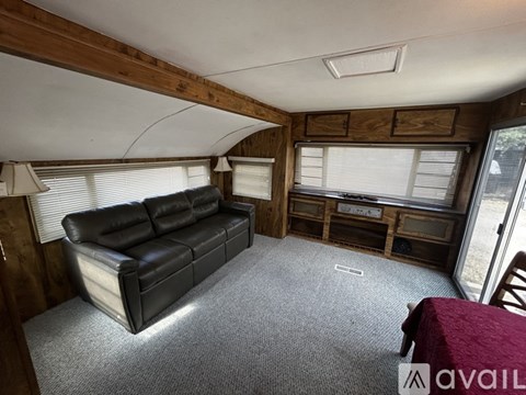 A living room with a black leather couch and wooden walls.