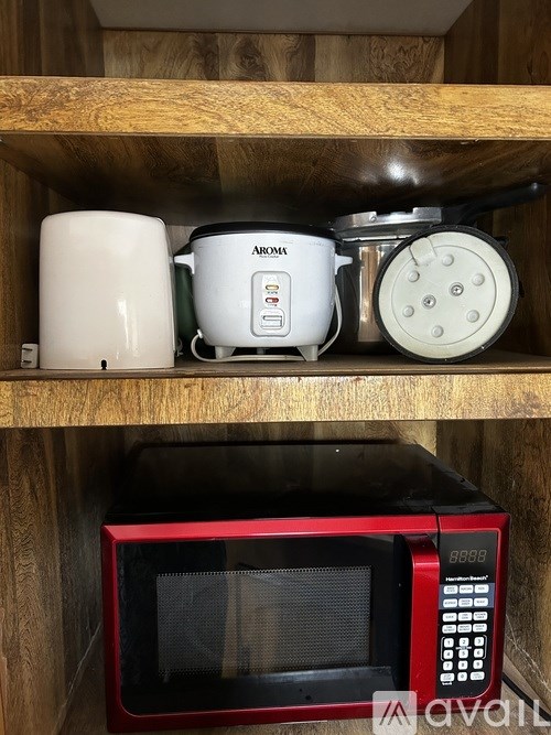 A red microwave oven is on a shelf above a black microwave oven.