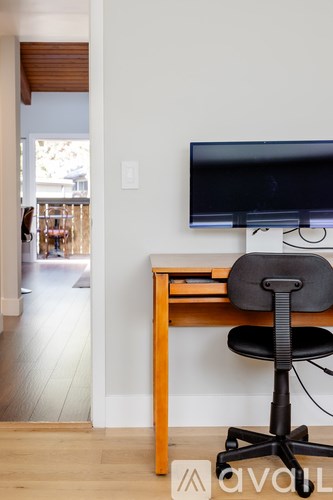 A black computer monitor is on a desk with a black chair.