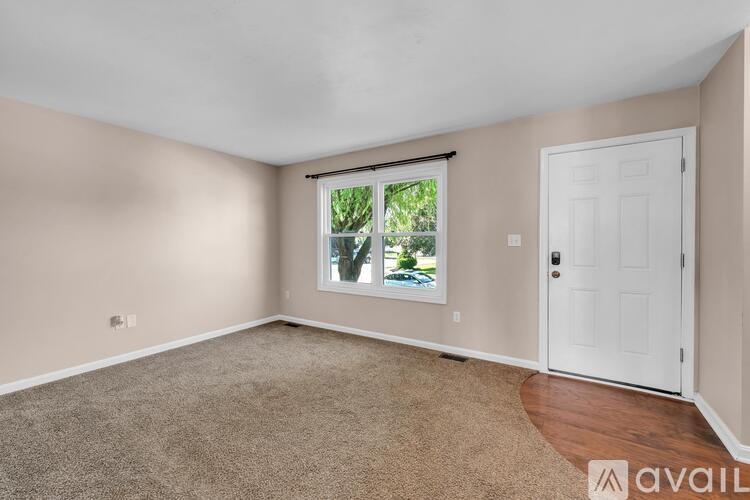 A room with a carpeted floor, a window with a view of trees, and a white door.