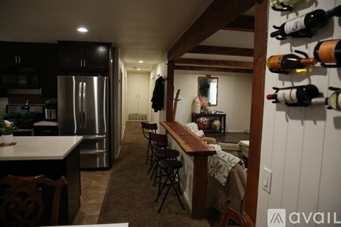A kitchen with a refrigerator, a dining table with chairs, and a wine rack with bottles.
