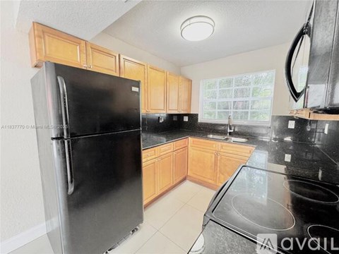 A black refrigerator in a kitchen with wooden cabinets.