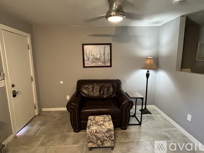 A living room with a brown leather couch, a small ottoman, and a floor lamp.