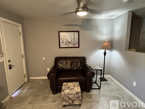 A living room with a brown leather couch, a small ottoman, and a floor lamp.