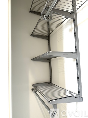 A metal shelving unit with three shelves is mounted on a white wall.