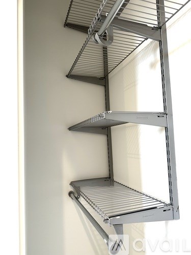 A metal shelving unit with three shelves is mounted on a white wall.