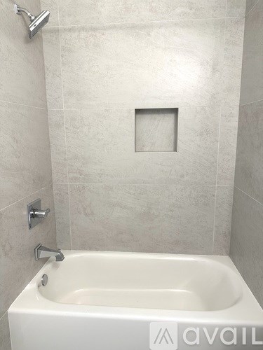 A white bathtub with a square hole in the wall behind it.