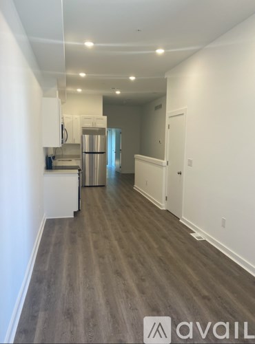 A kitchen with white cabinets and a refrigerator is visible through a doorway.