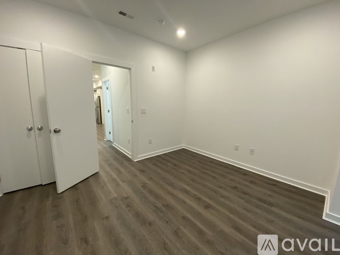 A room with wooden flooring and white walls, with a door on the left and a mirror on the right.