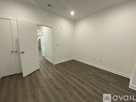A room with wooden flooring and white walls, with a door on the left and a mirror on the right.