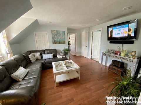 A living room with a black leather couch and a television mounted on the wall.