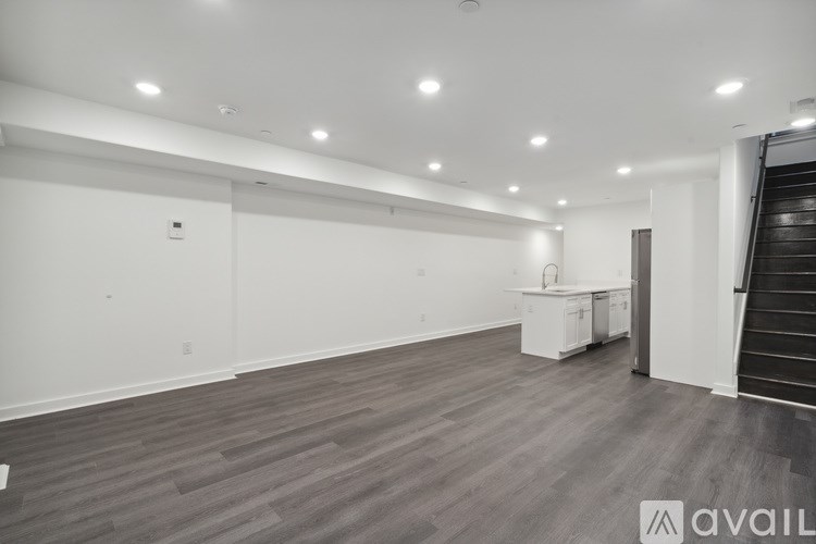 A spacious room with wooden flooring and a staircase on the right side.
