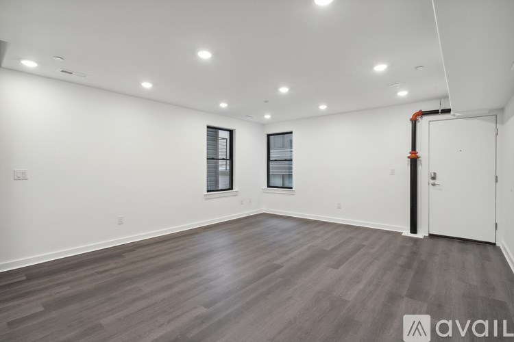 A spacious room with wooden flooring and two windows.