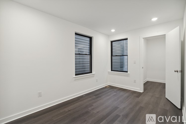 A room with wooden flooring and two windows with blinds.