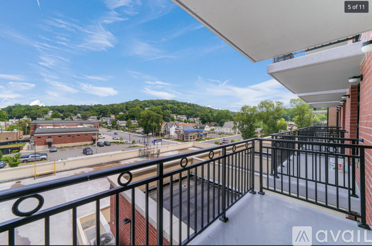 A balcony with a black railing overlooks a parking lot and buildings.