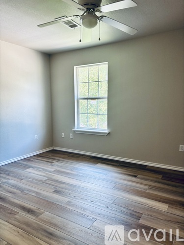 A room with a ceiling fan and a window with a view of trees.