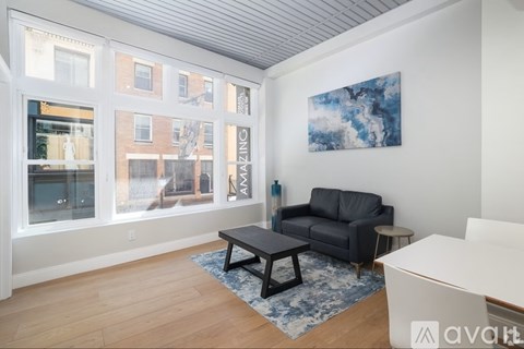 A living room with a black couch and a painting on the wall.