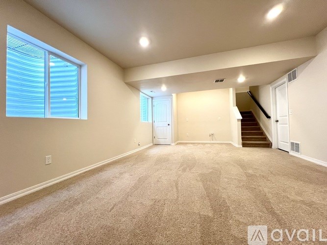 A spacious room with carpeted floor, a staircase, and a window with blinds.