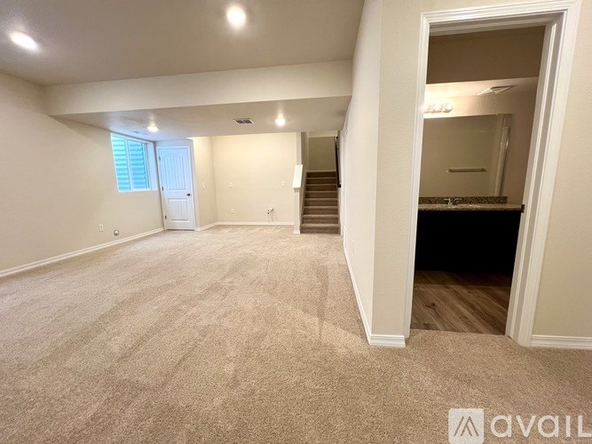A spacious room with beige carpeting and a staircase leading to another room.
