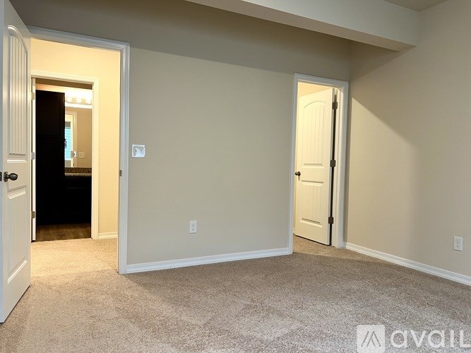 A room with beige walls and carpet flooring, with two doors and one window.