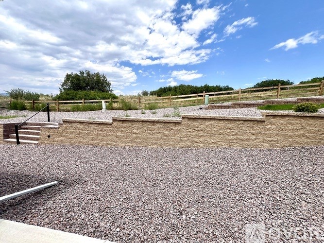 A gravel area with a wooden fence and a bench.
